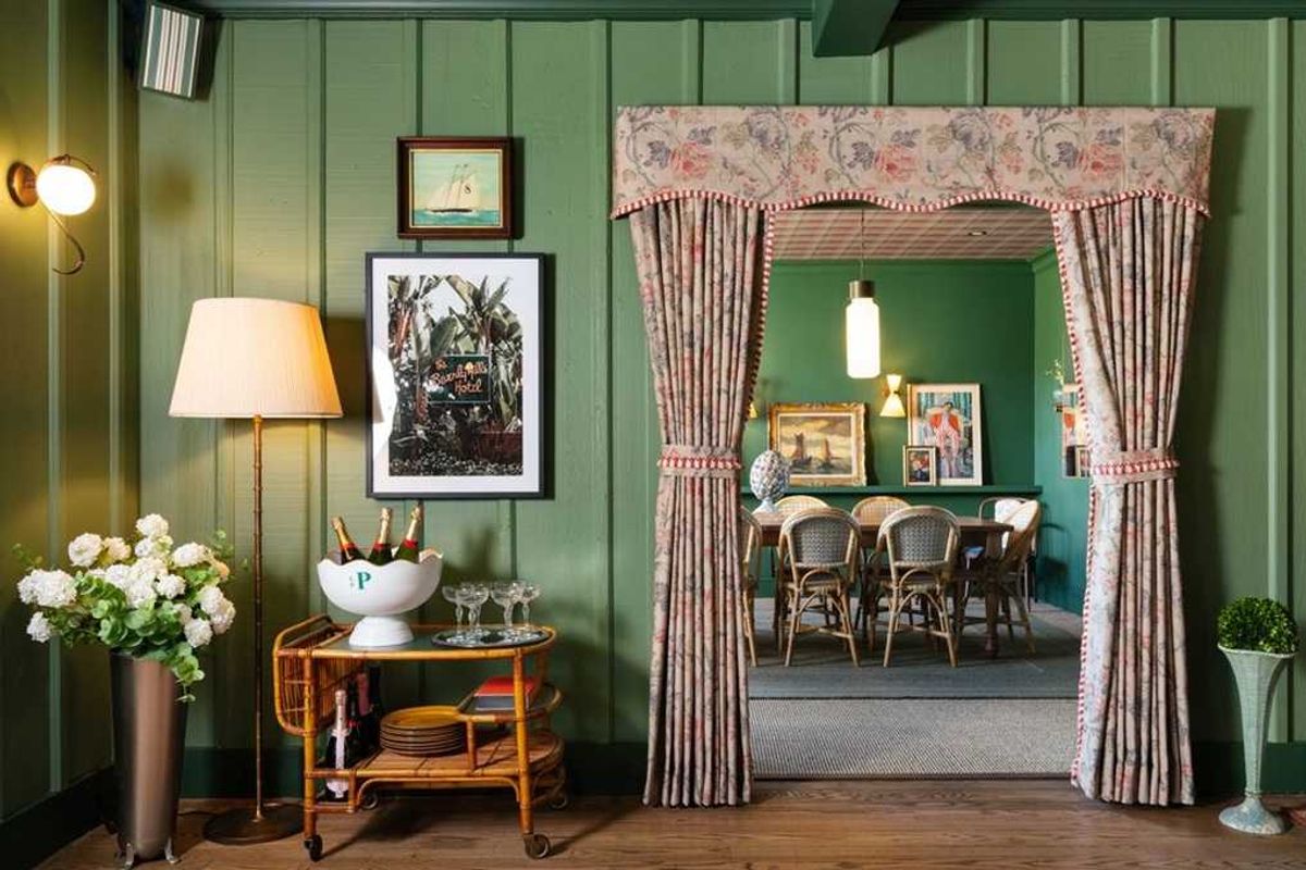 Stylish green room with floral curtains, art, and elegant dining setup.