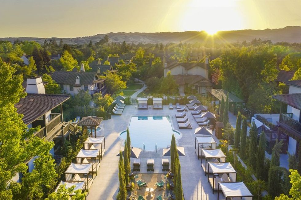 Sunlit resort with a central pool, surrounded by cabanas and lush greenery at sunset.