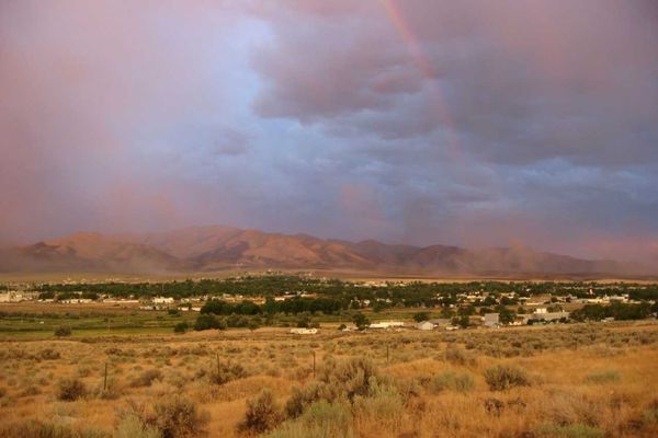 Sunset over a small town with mountains, a light rainbow, and vibrant skies.