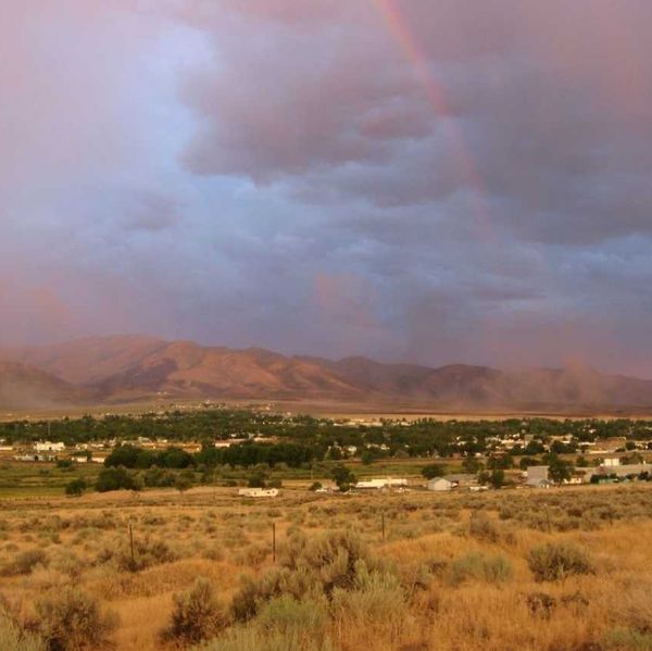 Sunset over a small town with mountains, a light rainbow, and vibrant skies.