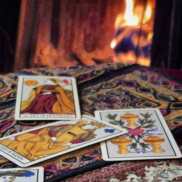 tarot cards on a table with a colorful tablecloth in front of a fireplace