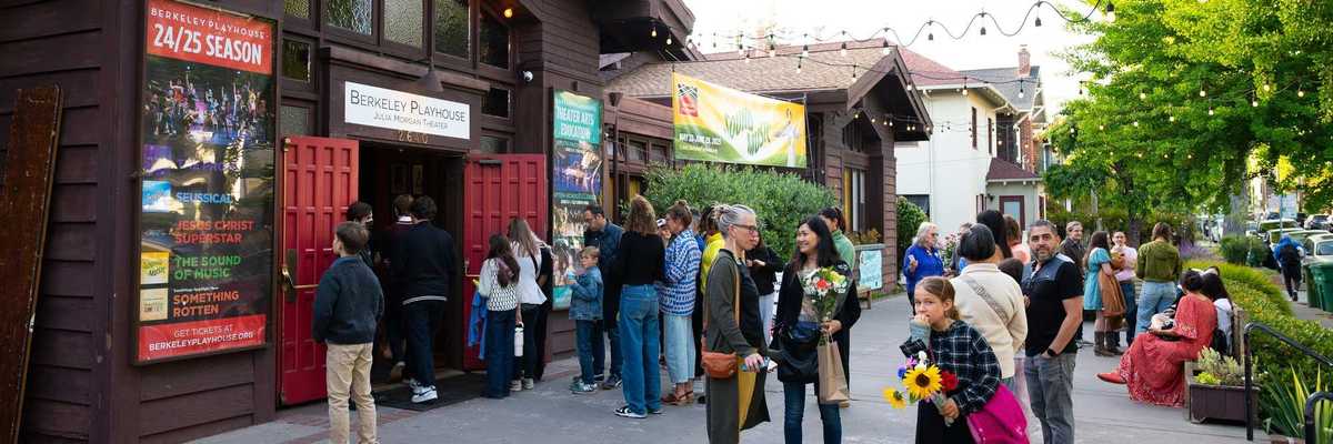 the front of a theater with a plaza in front and people standing around