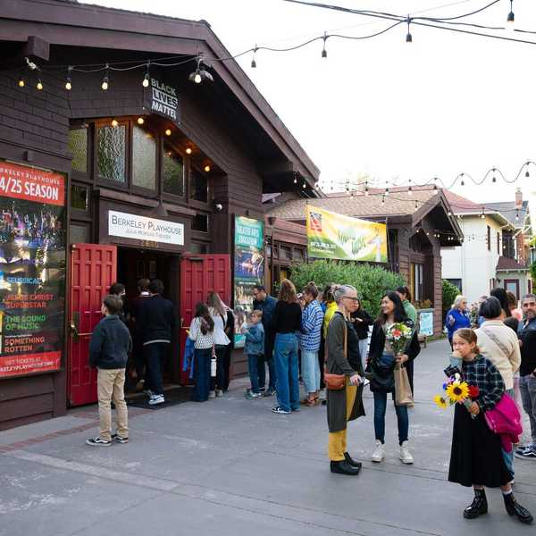 the front of a theater with a plaza in front and people standing around