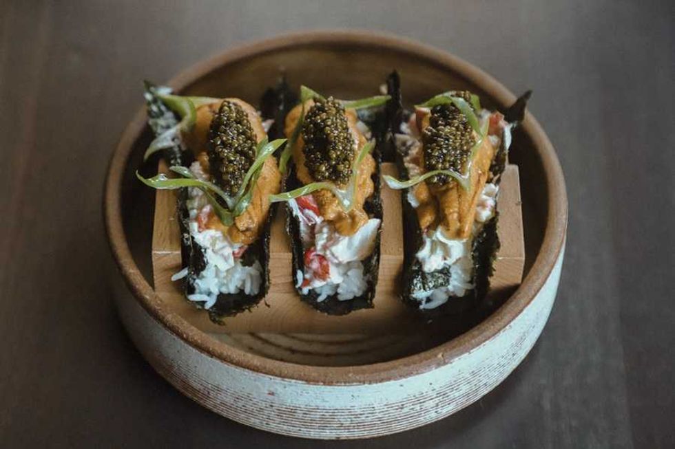 Three gourmet sushi tacos with seaweed, crab, uni, and caviar, served in a round dish.
