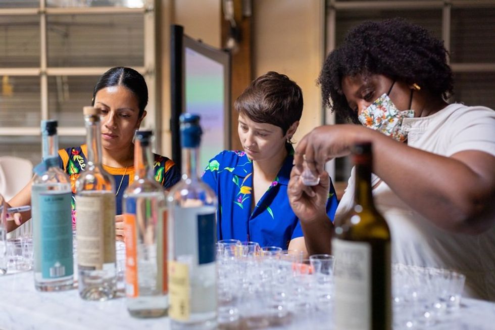 Three people preparing drinks at a table with bottles and cups.