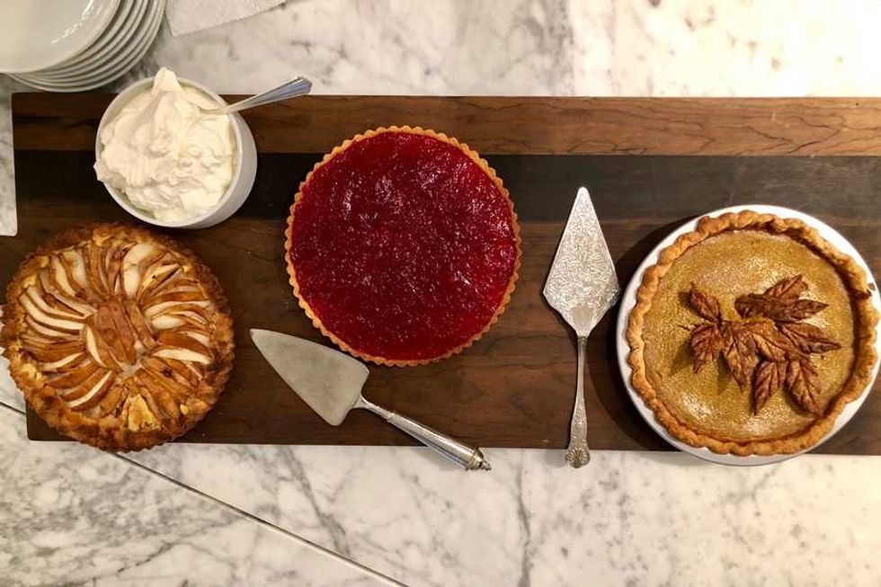Three pies and whipped cream on a wooden board with serving utensils.