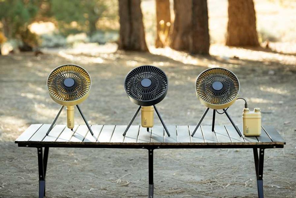 Three portable fans on a wooden table in a forest setting.