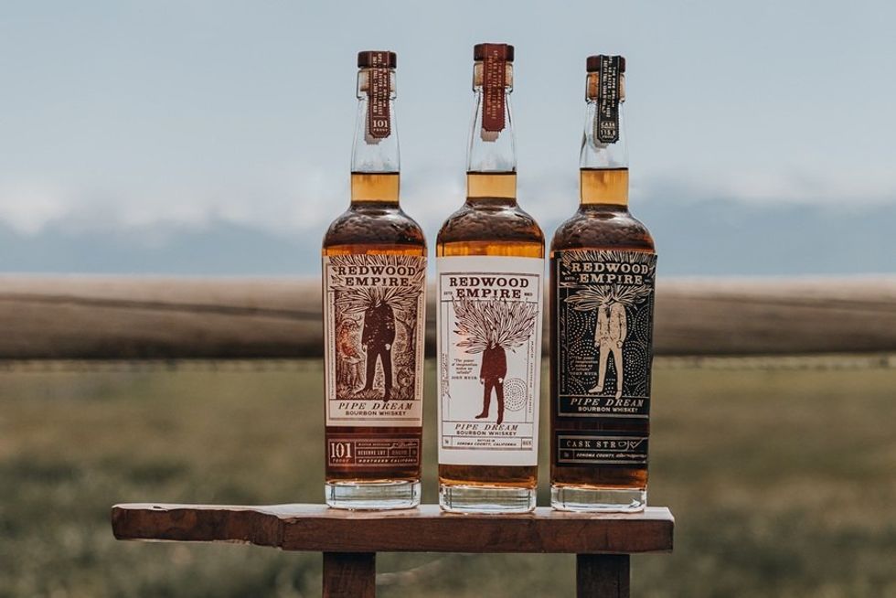 Three Redwood Empire whiskey bottles on a wooden table with a scenic background.