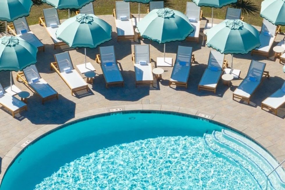 Turquoise pool with sun loungers and teal umbrellas arranged around it.
