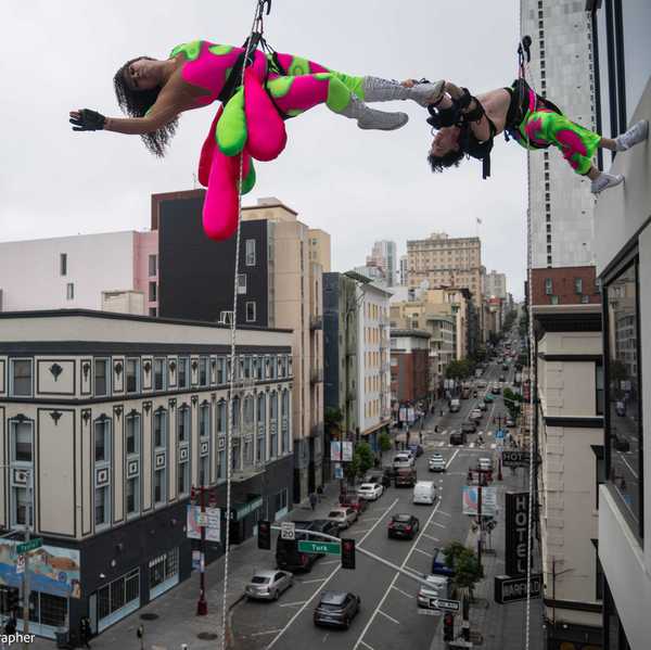 two acrobats in green and pink clothing hanging from the side of a tall building