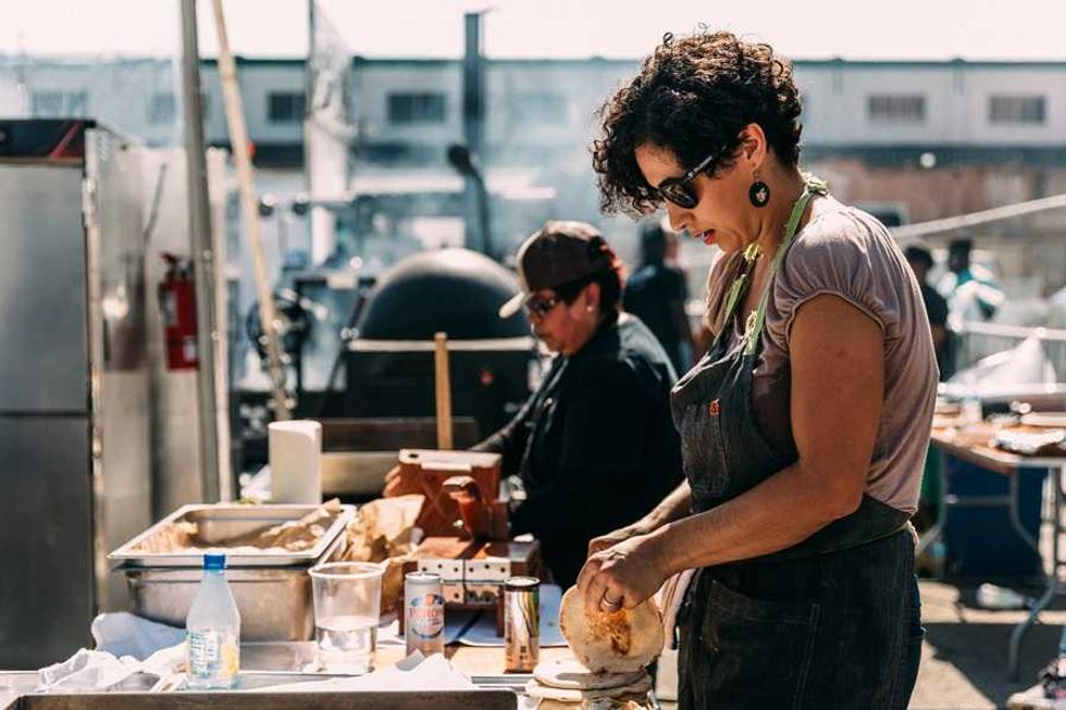 Two chefs preparing food outdoors at a busy market or festival.