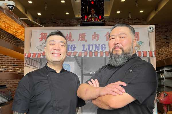 two Chinese American men smiling in front of a handpainted sign