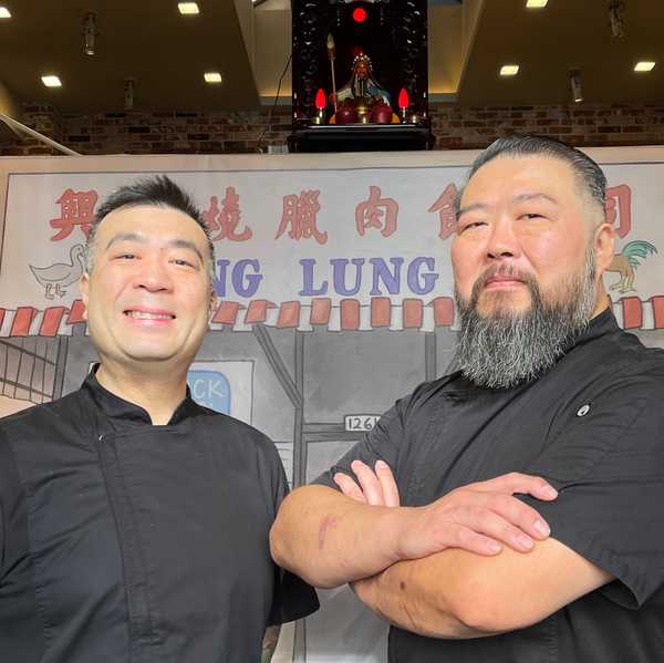 two Chinese American men smiling in front of a handpainted sign