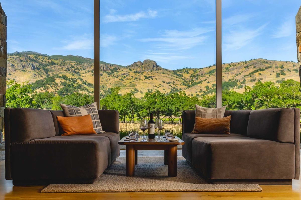 two couches with a coffee table with wine and wine glasses and a large window with a view of Napa