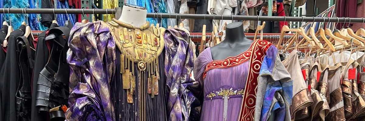 two elaborate costumes from the opera stage in front of racks of hundreds more