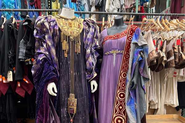 two elaborate costumes from the opera stage in front of racks of hundreds more