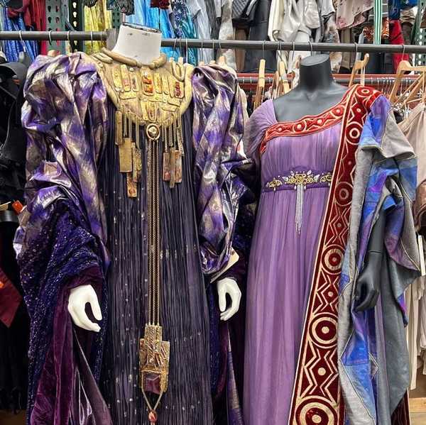 two elaborate costumes from the opera stage in front of racks of hundreds more