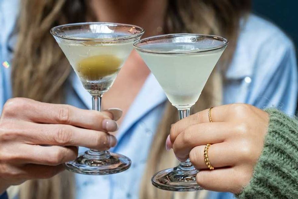 Two hands clinking martini glasses, one with an olive.