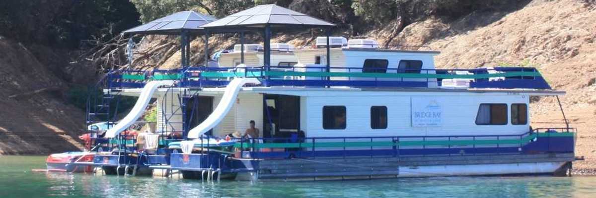 two house boats anchored at a beach with trees on the slope above