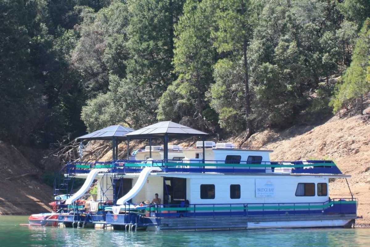 two house boats anchored at a beach with trees on the slope above