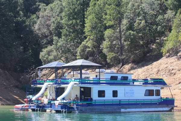 two house boats anchored at a beach with trees on the slope above