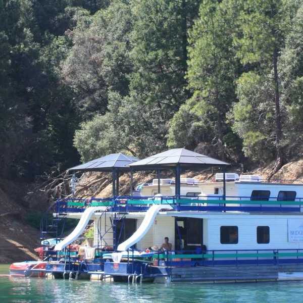 two house boats anchored at a beach with trees on the slope above