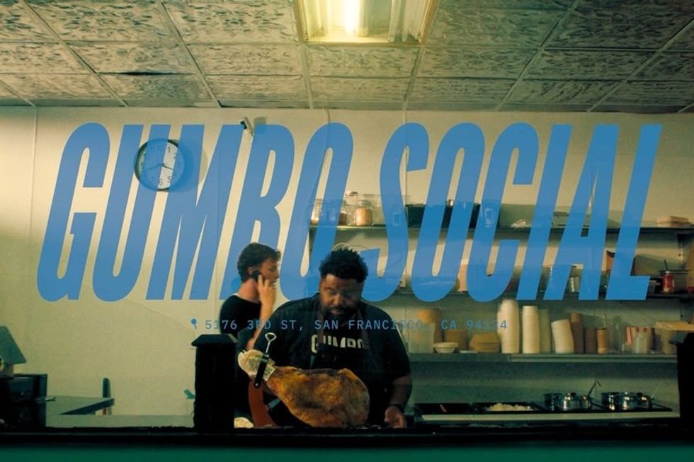 Two men working in a kitchen behind "Gumbo Social" window text.