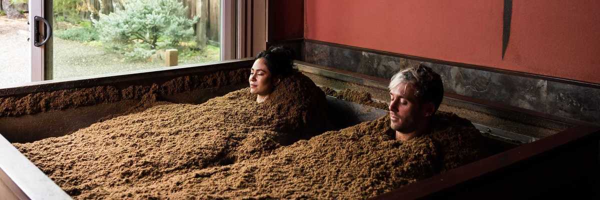 two people buried in sawdust to their necks in a room with Japanese symbols on the wall
