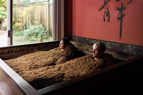 two people buried in sawdust to their necks in a room with Japanese symbols on the wall