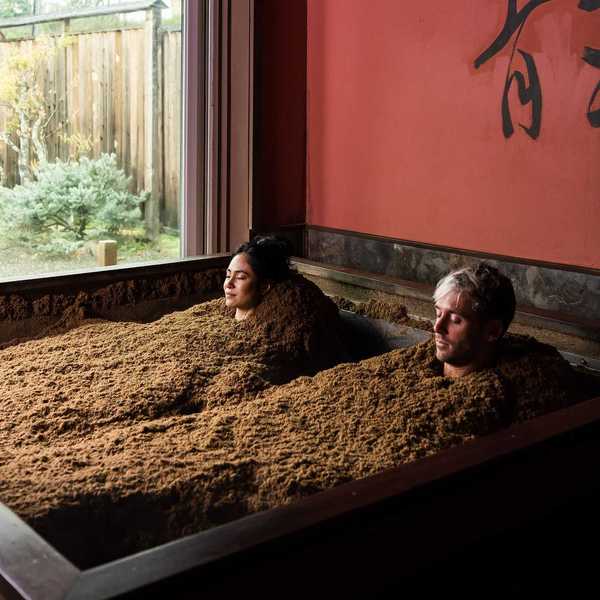 two people buried in sawdust to their necks in a room with Japanese symbols on the wall