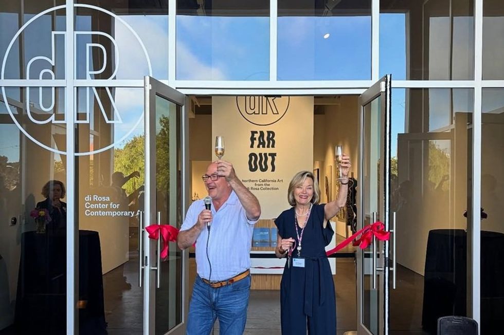 Two people celebrate with a ribbon cutting at a gallery entrance.