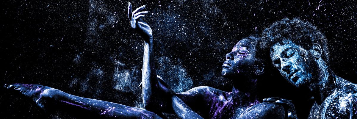 Two people covered in blue and purple powder in a dark, starry environment.