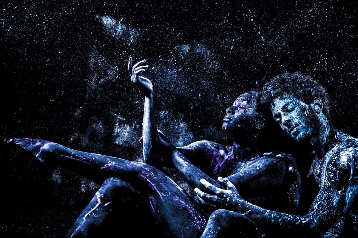 Two people covered in blue and purple powder in a dark, starry environment.