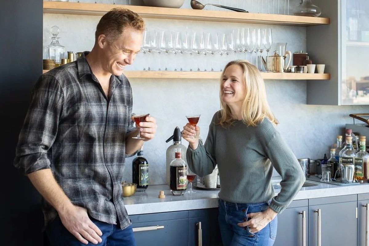 Two people drink amaro cocktails in a kitchen.