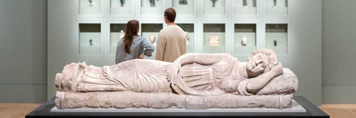 two people looking at artifacts in a museum with a prostrate sculpture in the foreground
