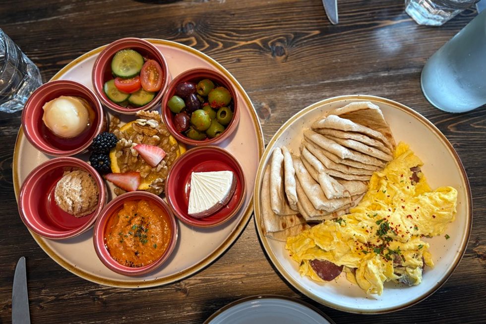 Two plates of breakfast items including eggs, pita bread, olives, and assorted dips.