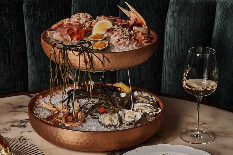 Two-tier seafood platter with a glass of white wine on a marble table.