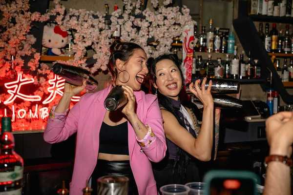 two women bartenders shaking cocktail shakers and looking at eachother with big smiles