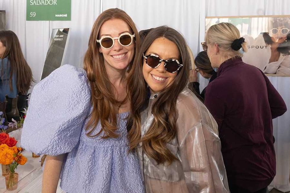 Two women smiling and wearing sunglasses at a lively indoor event.