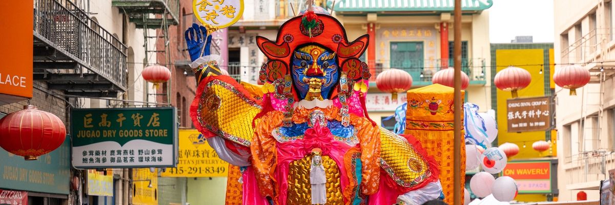 Vibrant Chinese festival with a giant colorful deity figure and red lanterns overhead.