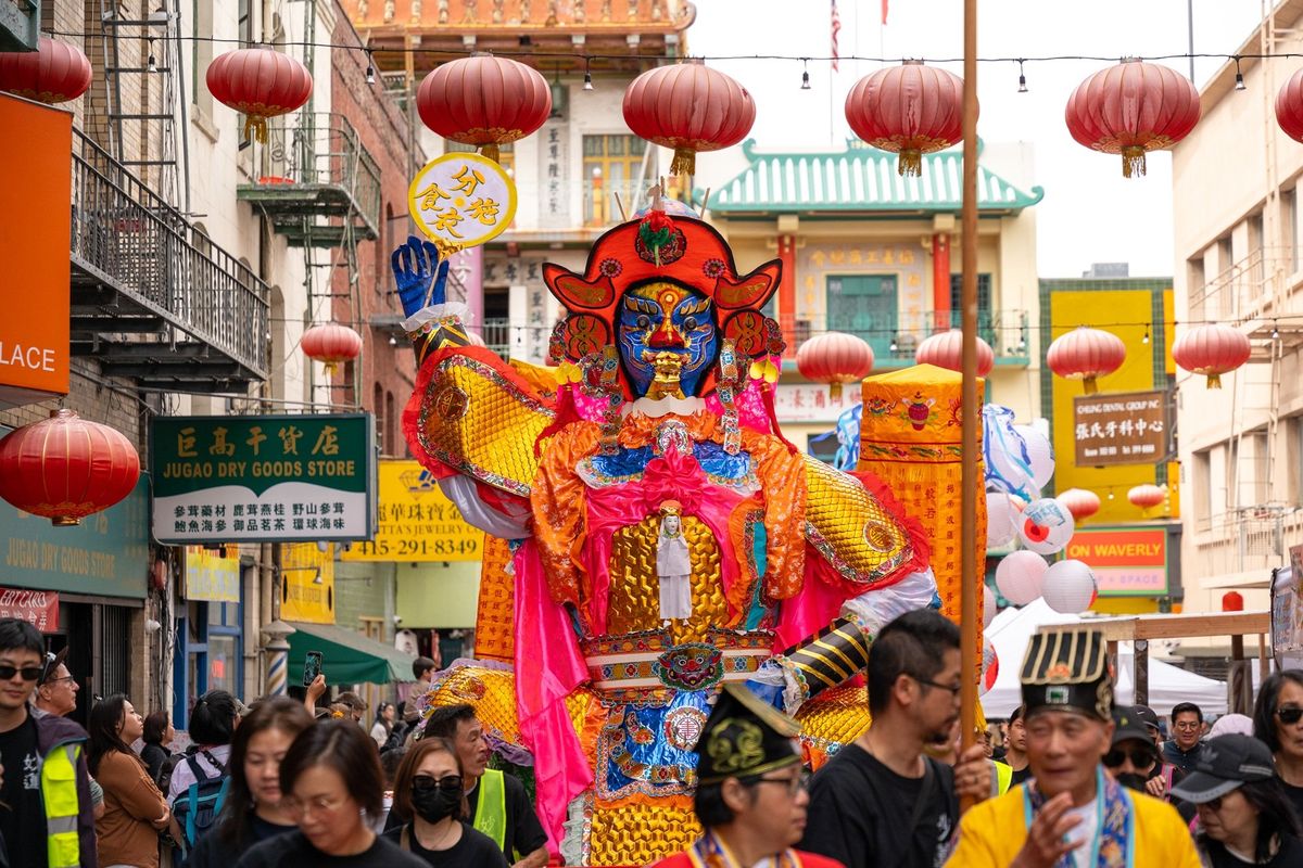 Vibrant Chinese festival with a giant colorful deity figure and red lanterns overhead.