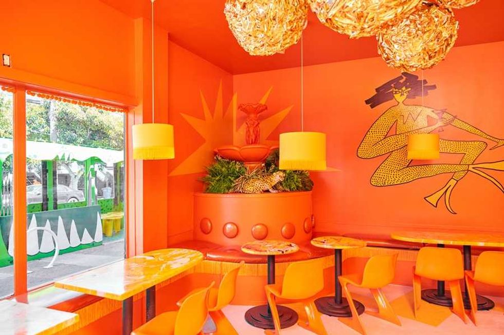 Vibrant orange cafe with bold artwork, unique lamps, and modern seating.