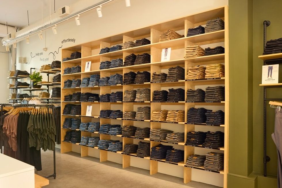 Wall of neatly stacked pants in various colors in a brightly lit clothing store.