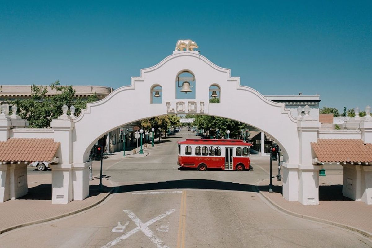 White archway with a red trolley passing under, clear blue sky above.