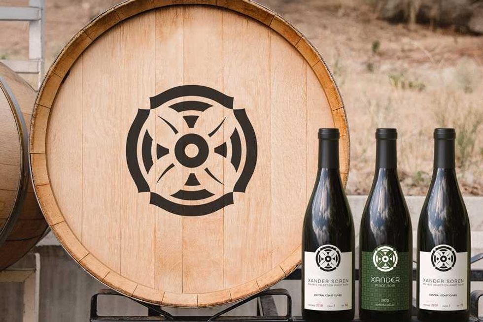 Wine barrel with logo and three bottles labeled "Xander Soren" on a vineyard background.