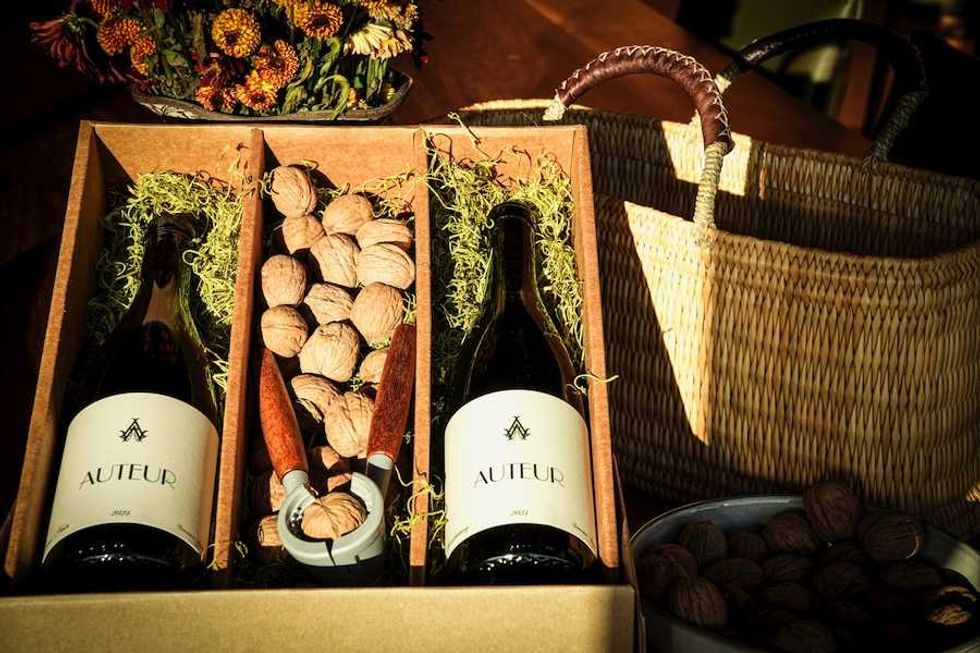 Wine bottles and walnuts in a gift box with a nutcracker and wicker basket nearby.
