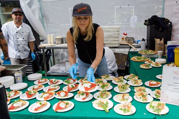 Woman assembling plates of pizza slices at a food stall with helpers.