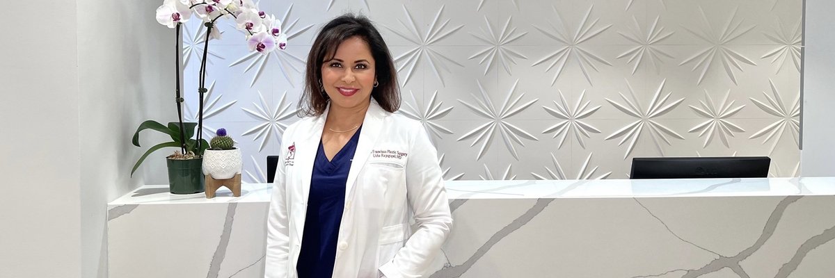 Woman in a white coat stands at modern, stylish reception desk with orchid decoration.