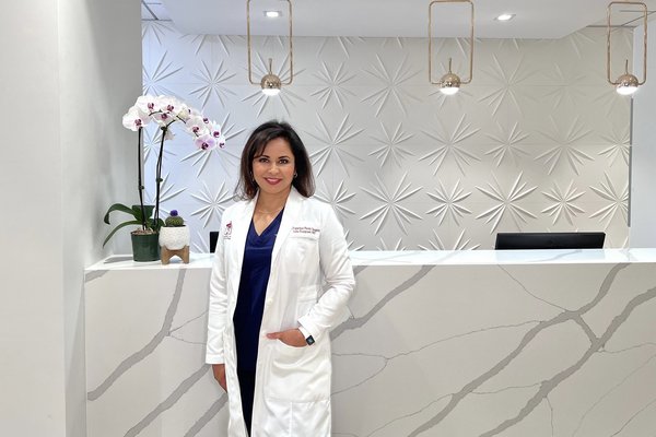 Woman in a white coat stands at modern, stylish reception desk with orchid decoration.