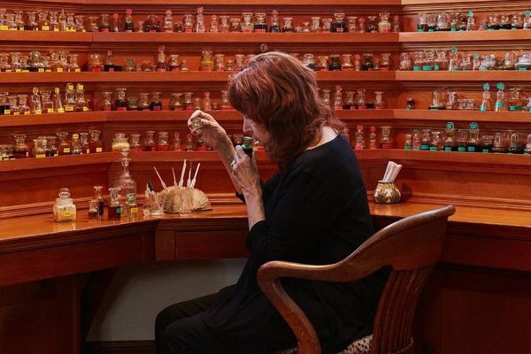 Woman sitting at a wooden desk surrounded by shelves of small bottles.